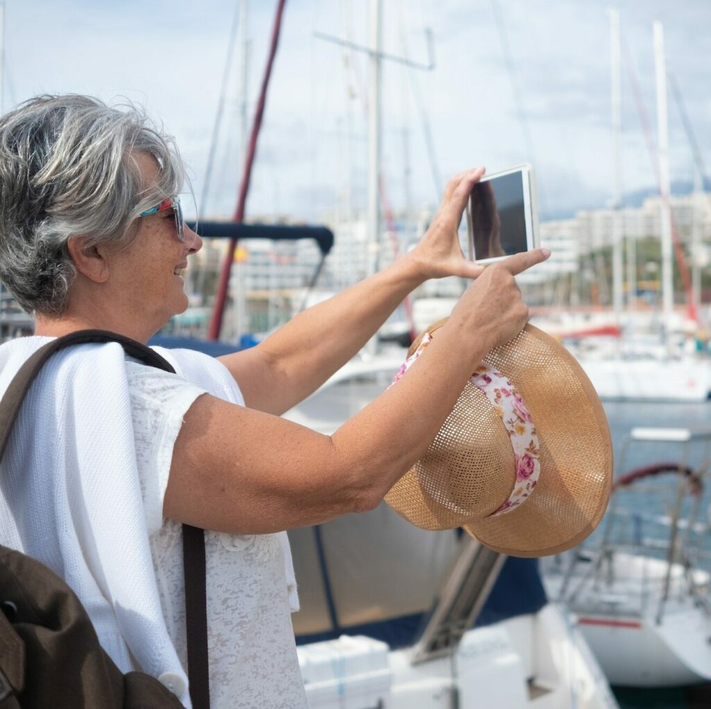 A port with yachts and sailboats. An elderly woman with gray hairs takes a photo at the scenary