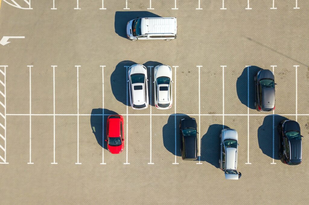 Aerial view of many colorful cars parked on parking lot with lines and markings for parking places