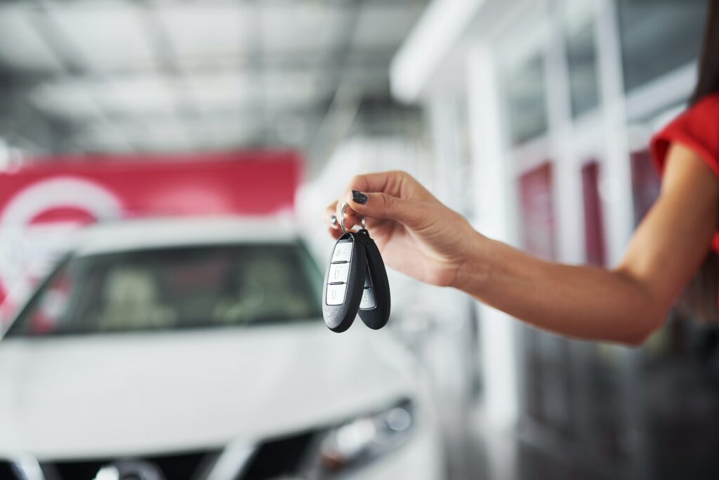 Cropped closeup of a car dealer holding out car keys to the camera at car dealership salon